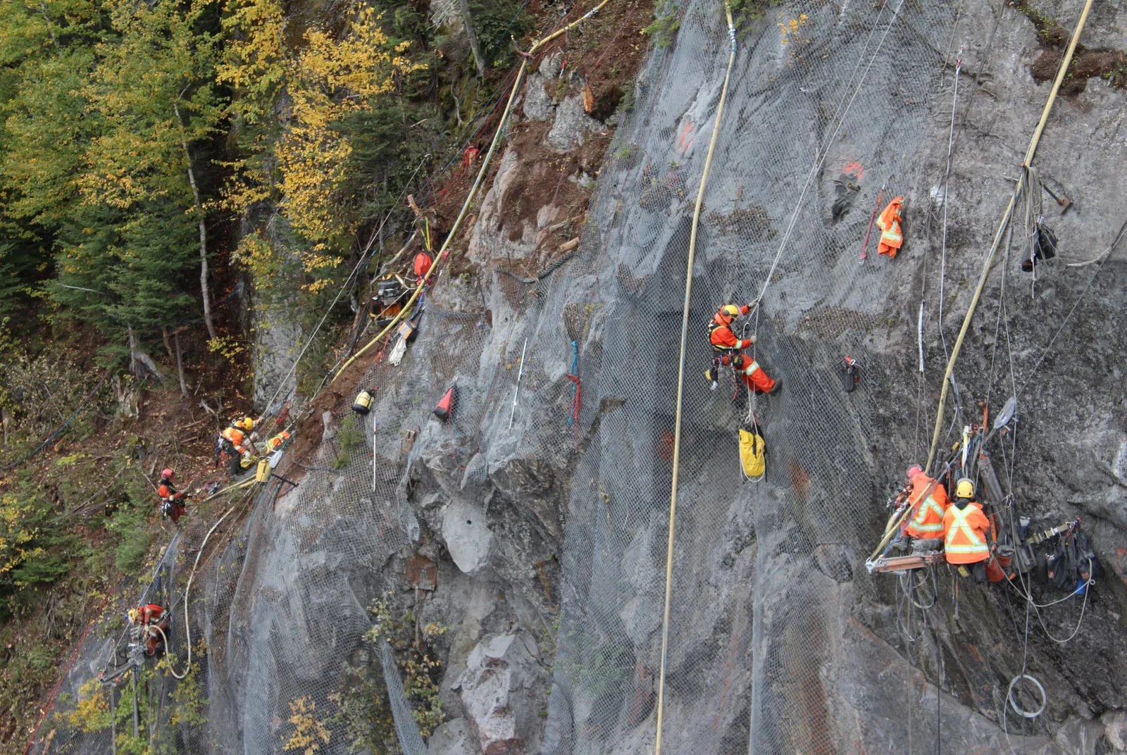Équipe installant des boulons d’ancrage et un treillis métallique sur une paroi rocheuse.